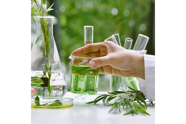Image Hand in a white coat doing a chemistry experiment, holding glass with green liquid.